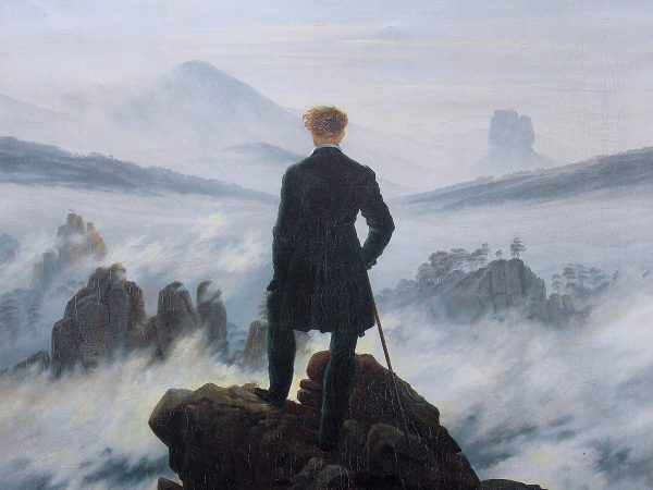 Man with a walking stick on a rocky summit gazing over fog-covered mountains